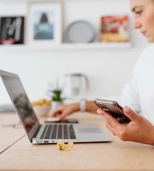 Woman checking a booking on her phone next to a laptop